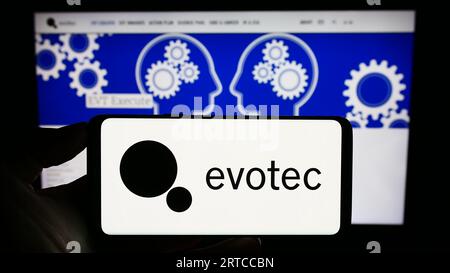 Person holding cellphone with logo of German drug discovery company Evotec SE on screen in front of business webpage. Focus on phone display. Stock Photo