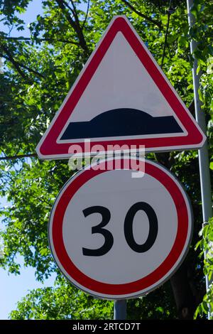 rough road sign and speed limit on a background of green trees and blue sky. Stock Photo