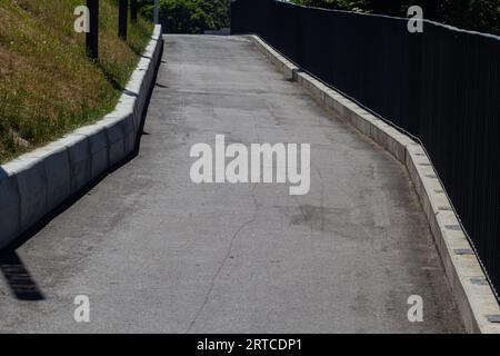 The edge of a park paved road, separated by a curb with a lawn. Fallen yellow autumn leaves on the road and lawn. Spots of light on the road. Stock Photo