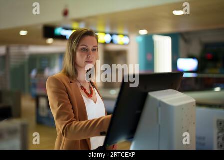 Woman checks her flight at self-service terminal at the airport. Stock Photo