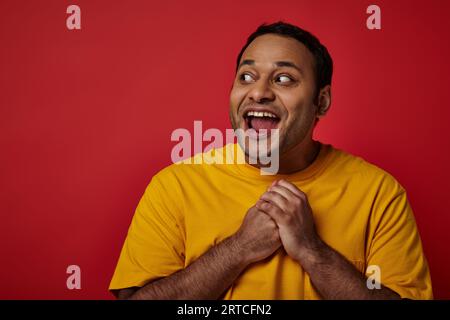 astonished indian man with wide eyes open looking away on red background in studio, surprise concept Stock Photo