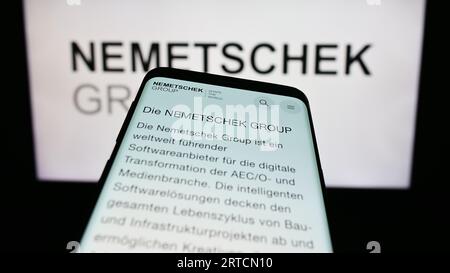 Mobile phone with webpage of German software company Nemetschek SE on screen in front of business logo. Focus on top-left of phone display. Stock Photo