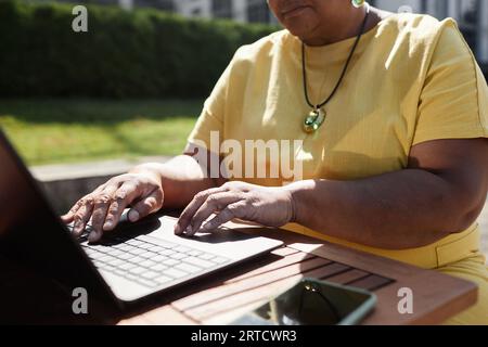 Closeup of mature Black woman using laptop outdoors in sunlight focus on hands typing, copy space Stock Photo