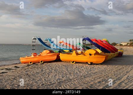 View of pretty colorful pedal boats on the sandy beach of Alcudia illuminated by the morning sun Stock Photo