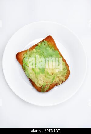 Avocado pasta on fried toast. Vegetables spread on bread. Vegan breakfast on a white plate. Stock Photo