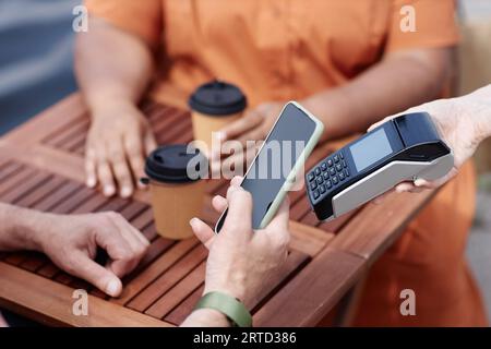 Closeup of unrecognizable person paying via NFC by smartphone at outdoor cafe, copy space Stock Photo