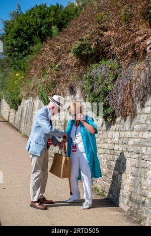 elderly couple smartly dressed looking in a bag and talking while out for a walk together on a sunny day. Stock Photo