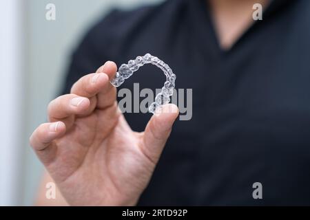 Dentist in black uniform holding clear aligners of orthodontic treatment tool for teeth care Stock Photo