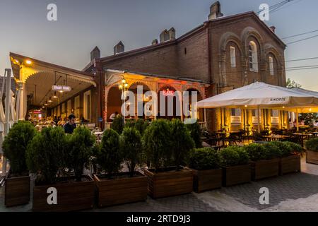 Guests sit in the outdoor area of the Kikodze Coffee & Cocktail Bar. The building is illuminated. A bar sign is lit up. The scene takes place in Vardisubani, Tbilisi, Georgia Stock Photo