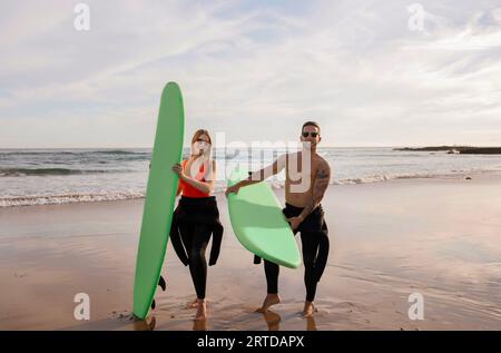 Young man and woman with surfboards posing on the beach at sunset Stock Photo