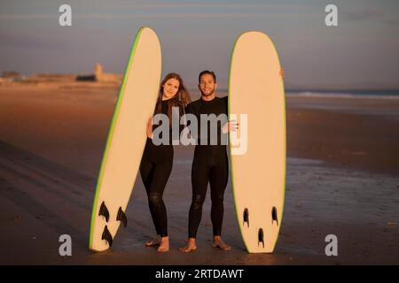 Beautiful Surfers Couple With Two Surfboards Posing On The Beach At Sunset Stock Photo