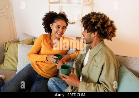 Cheerful Black Spouses Talking Having Coffee on Sofa At Home Stock Photo