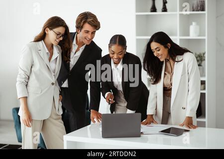 Teamwork success. Happy diverse office workers looking at laptop, interacting and discussing work indoors in office Stock Photo