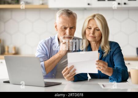 Senior Couple Checking Financial Documents While Sitting In Kitchen At Home Stock Photo