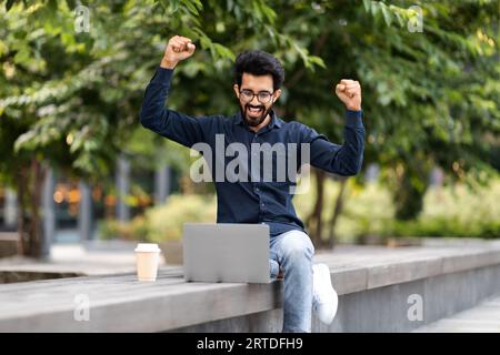 Excited eastern entrepreneur working remotely on the street, using laptop Stock Photo