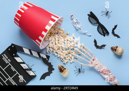 Composition with tasty popcorn, clapperboard, 3D glasses and Halloween decor on blue background Stock Photo