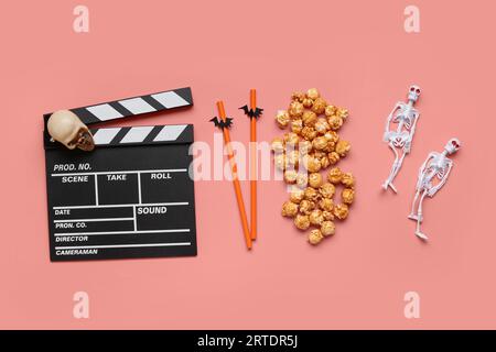 Composition with tasty caramel popcorn, clapperboard, skull, skeletons and straws for Halloween celebration on coral background Stock Photo