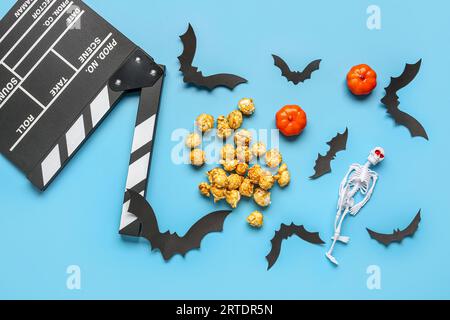 Composition with tasty caramel popcorn, clapperboard, paper bats, skeleton and pumpkins for Halloween celebration on blue background Stock Photo