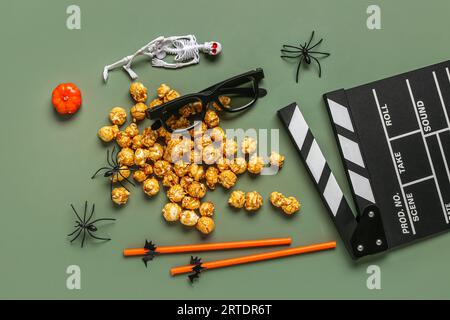 Composition with tasty caramel popcorn, clapperboard, 3D glasses, straws and spiders for Halloween celebration on green background Stock Photo