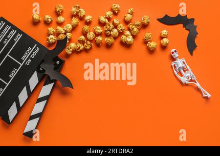 Composition with tasty caramel popcorn, clapperboard, paper bats and skeleton for Halloween celebration on orange background Stock Photo