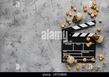 Movie clapperboard with caramel popcorn and Halloween skulls on grey grunge background Stock Photo