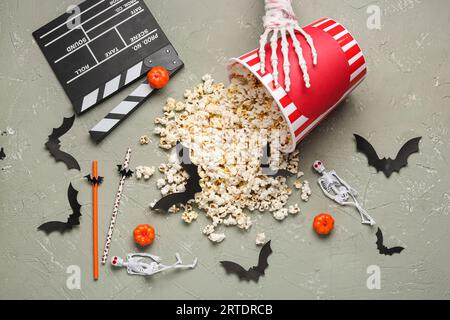 Overturned bucket with popcorn, movie clapperboard and Halloween decor on grey grunge background Stock Photo