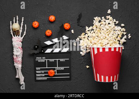 Overturned bucket with popcorn, movie clapperboard and Halloween decor on black grunge background Stock Photo