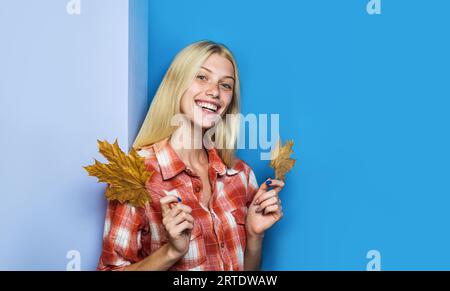 Smiling blonde girl in plaid shirt with autumn leaves. Happy autumn woman in casual wear with maple leaf. Fashion female model with fall foliage Stock Photo