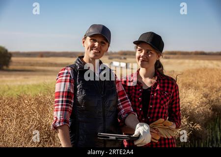 Close-up portrait of a woman farmer and her apprentice standing in the fields with grain haulers in the background, while teaching her about modern... Stock Photo