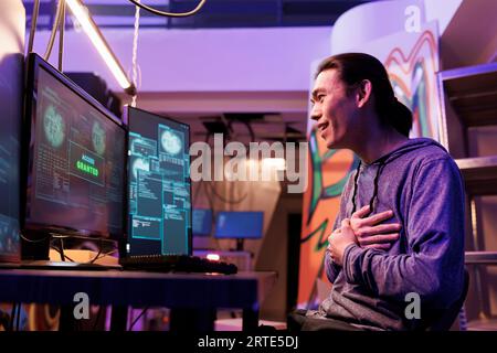 Excited hacking system successfully while doing illegal activities in abandoned warehouse. Happy shocked young asian criminal getting access granted message on computer screen Stock Photo