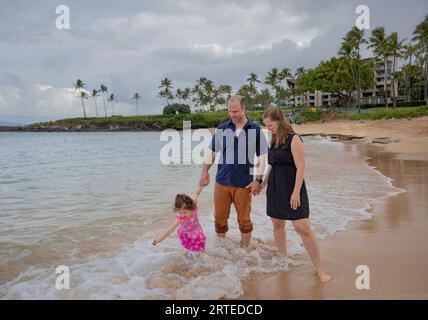 Family going for a walk on the beach, standing in the water along the surf on the shore at Kapalua Resort in West Maui Stock Photo