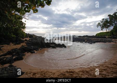View of Secret Beach looking out at the cove along the rocky shore of the Pacific Ocean at twilight; Makena, Maui, Hawaii, United States of America Stock Photo
