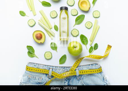 Green fruit, vegetables and smoothie fall in jeans with yellow tape measure as belt Stock Photo