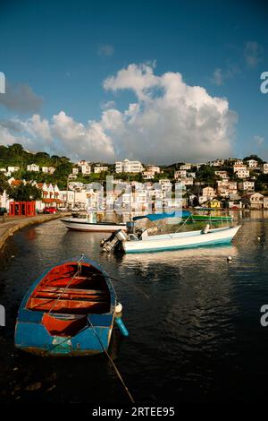 Harbor scene with colorful fishing boats moored close to shore and the port city capital of St Georges in the background on a sunny day Stock Photo