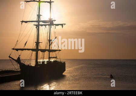 Silhouette of people onboard a tall ship moored to the dock in the Cayman Islands capital city of George Town with kayakers along side paddling out... Stock Photo