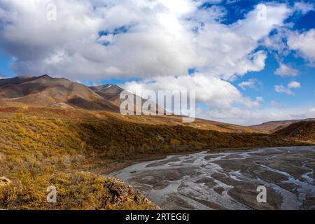 Sunny and cloudy autumn day along the East Fork Toklat River and river bed, with the fall coloured tundra on the Alaska Range Mountains rising in t... Stock Photo