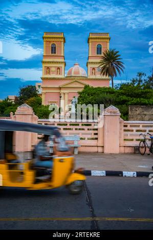 Auto rickshaw on a road in Pondicherry, India, travelling on a street passing by a church building; Pondicherry, Tamil Nadu, India Stock Photo