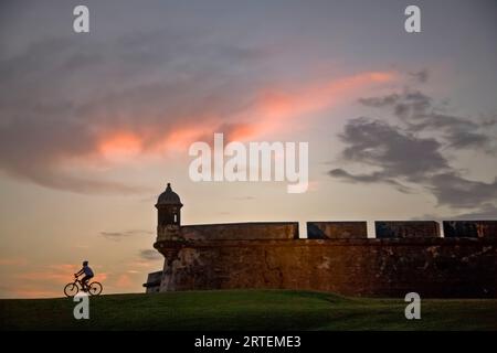 Silhouette of a cyclist and San Felipe del Morro Castle at sunset; San Juan, Puerto Rico Stock Photo