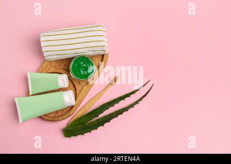 Tubes of toothpaste, fresh aloe, toothbrush and towel on pink background, flat lay. Space for text Stock Photo