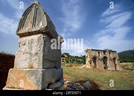 Roman-triple-arched gateway, built in 100 AD, with a stone structure in foreground; Patara, Turkey Stock Photo
