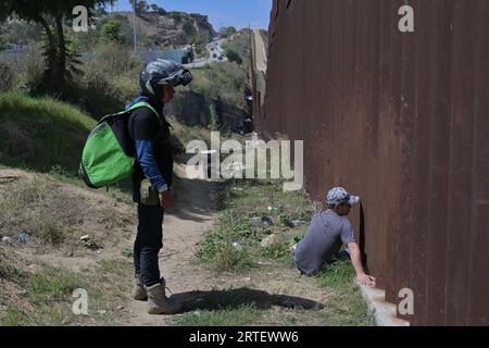 Tijuana, Baja California, Mexico. 12th Sep, 2023. Around a hundred people are stuck between the two US-Mexico border fences dividing Tijuana and San Diego on Tuesday, September 12, 2023, as viewed from Tijuana, Mexico. The migrants are from countries in South America, Central Asia, Eastern Europe and Africa. All are seeking a chance to enter the US via asylum status, as some lost patience in the process of getting appointments through the CBP One application and crossed illegally out of desperation, some waiting months. Migrants claim that the appointment system is over saturated and is di Stock Photo