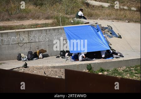 Tijuana, Baja California, Mexico. 12th Sep, 2023. Around a hundred people are stuck between the two US-Mexico border fences dividing Tijuana and San Diego on Tuesday, September 12, 2023, as viewed from Tijuana, Mexico. The migrants are from countries in South America, Central Asia, Eastern Europe and Africa. All are seeking a chance to enter the US via asylum status, as some lost patience in the process of getting appointments through the CBP One application and crossed illegally out of desperation, some waiting months. Migrants claim that the appointment system is over saturated and is di Stock Photo