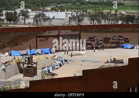 Tijuana, Baja California, Mexico. 12th Sep, 2023. Around a hundred people are stuck between the two US-Mexico border fences dividing Tijuana and San Diego on Tuesday, September 12, 2023, as viewed from Tijuana, Mexico. The migrants are from countries in South America, Central Asia, Eastern Europe and Africa. All are seeking a chance to enter the US via asylum status, as some lost patience in the process of getting appointments through the CBP One application and crossed illegally out of desperation, some waiting months. Migrants claim that the appointment system is over saturated and is di Stock Photo