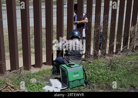 Tijuana, Baja California, Mexico. 12th Sep, 2023. Around a hundred people are stuck between the two US-Mexico border fences dividing Tijuana and San Diego on Tuesday, September 12, 2023, as viewed from Tijuana, Mexico. The migrants are from countries in South America, Central Asia, Eastern Europe and Africa. All are seeking a chance to enter the US via asylum status, as some lost patience in the process of getting appointments through the CBP One application and crossed illegally out of desperation, some waiting months. Migrants claim that the appointment system is over saturated and is di Stock Photo