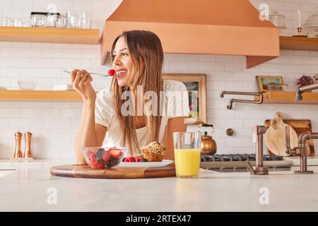 Smiling woman enjoying healthy breakfast in kitchen Stock Photo