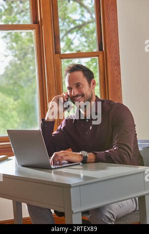 Smiling man using laptop and smart phone at table at home Stock Photo