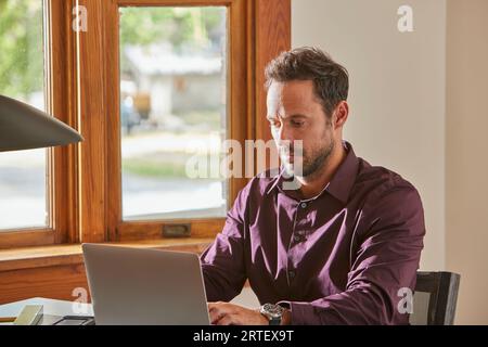 Man using laptop at desk at home Stock Photo