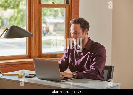 Man using laptop at desk at home Stock Photo