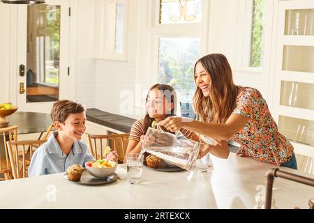 Smiling mother with son (8-9) and daughter (12-13) having breakfast in kitchen Stock Photo