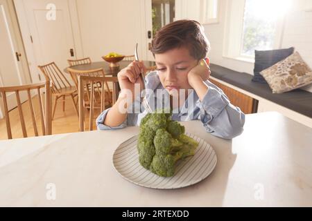 Displeased boy (8-9) looking at broccoli on plate in kitchen Stock Photo